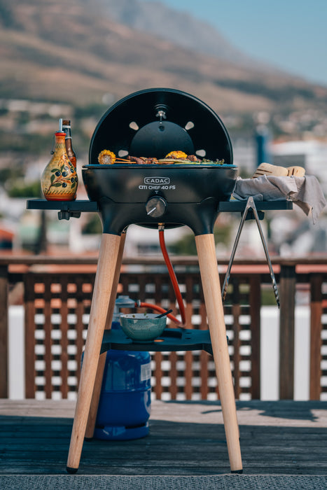 Cadac Citi Chef 40 FS Black - Urban & Camping Gas BBQ lifestyle image of side tables in use with oil and bread and sweetcorn and meat grilling with bowl on shelf