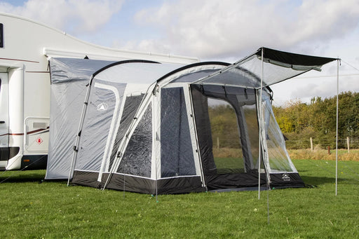 Sunncamp Swift 325 Tall Motorhome Porch Awning feature image of the awning pitch in a field on the side of a motorhome with trees in the background.  the front door is open and the right side door is unzipped. the porch door has canopy poles holding it up